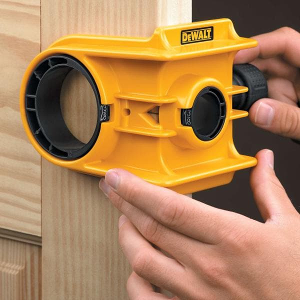 Eine Person verwendet ein gelbes DEWALT-Türschloss-Installationsset, um ein Loch an einem Türrahmen aus Holz auszurichten und zu markieren.