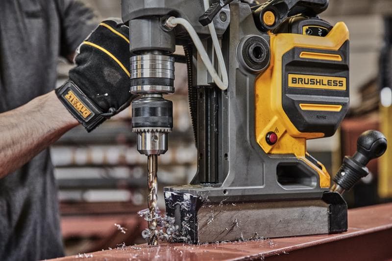 Person bohrt mit DEWALT bürstenloser Magnetbohrmaschine Löcher in Metall, Metallspäne liegen auf dem Tisch.