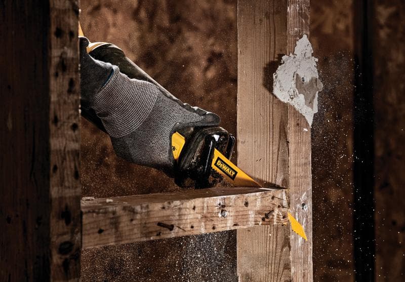 Nahaufnahme einer Hand mit grauem Handschuh, die eine DEWALT-Säbelsäge verwendet, um einen Holzbalken zu durchtrennen, während Sägespäne in die Luft fliegen.