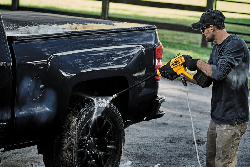 Eine Person verwendet einen kabellosen DEWALT DCPW550B Hochdruckreiniger, um das Rad und die Seite eines schwarzen Pick-up-Trucks im Freien zu reinigen.